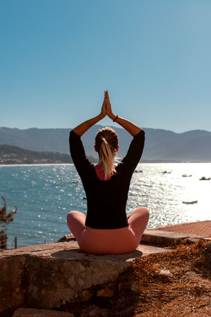 Woman practicing yoga by the water at sunrise, showing peace and balance